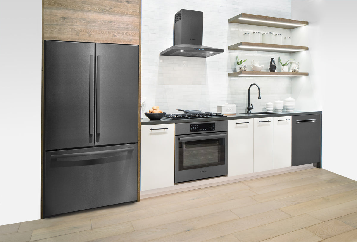 A modern kitchen setup featuring a large Bosch black stainless steel French-door refrigerator with a bottom freezer drawer, paired with white cabinets, a built-in Bosch range, a black stainless Bosch range hood, Bosch dishwasher, open wood shelves with glassware, and light wood flooring.